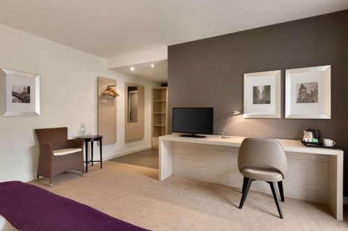 a room with a desk with a television and chairs at Ramada by Wyndham München Airport in Oberding