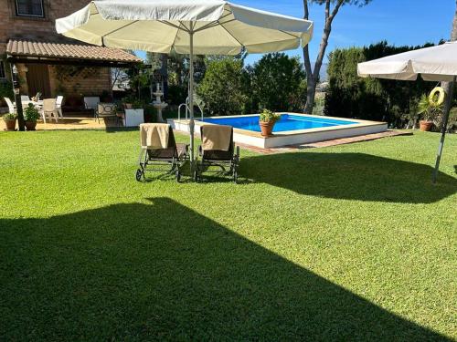 zwei Stühle und ein Sonnenschirm in einem Garten mit Pool in der Unterkunft Casa Rural Cupiana Piscina privada Malaga in Málaga