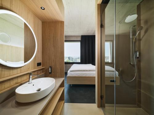 uma casa de banho com um lavatório, um chuveiro e uma cama. em Boulderbar Hotel Leonding em Linz