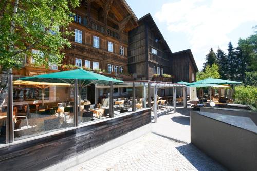 a restaurant with tables and umbrellas in front of a building at Schweizerhaus Swiss Quality Hotel in Maloja