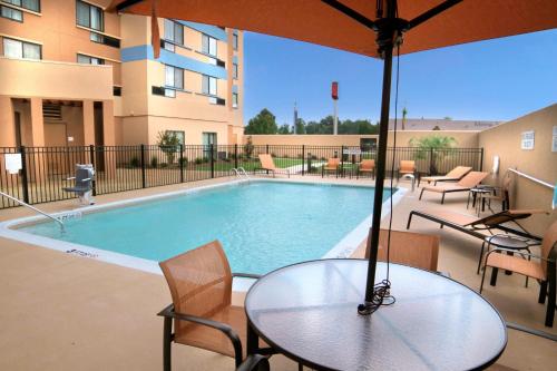 a swimming pool with a table and an umbrella at Courtyard by Marriott Jackson Airport/Pearl in Pearl