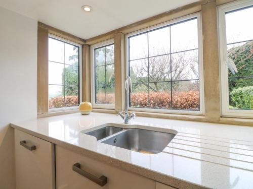 a kitchen with a sink and three windows at Fern Cottage in Bakewell