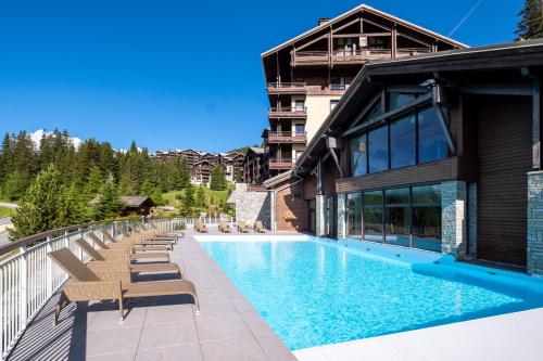 une piscine avec des chaises longues à côté d'un bâtiment dans l'établissement Résidence Pierre & Vacances Premium Les Terrasses d'Eos, à Flaine