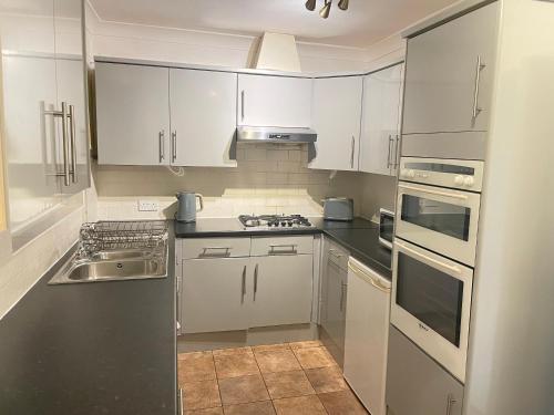 uma cozinha branca com armários brancos e um lavatório em Lovely 4 Bedroom House with 2 Bathroom, Garden and Private Parking em Thornton Heath