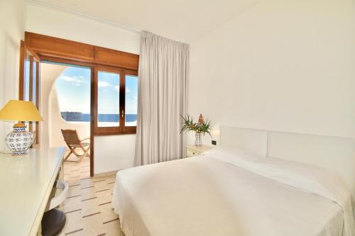 a white bedroom with a bed and a window at Cossyra Hotel in Pantelleria