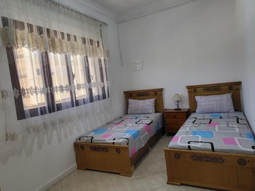 two twin beds in a room with two windows at Appartement Tanger 2 in Tangier