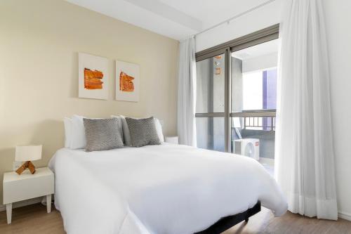a white bedroom with a large white bed and a window at Tabas - Z. Ibirapuera in Sao Paulo