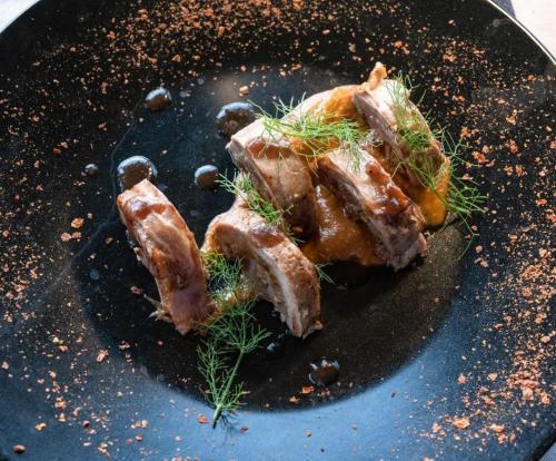 a piece of meat on a black plate with dill at Cossyra Hotel in Pantelleria