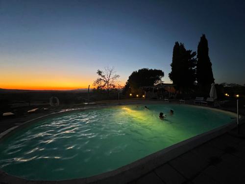 a group of people swimming in a pool at sunset at Antica Colombaia in Volterra