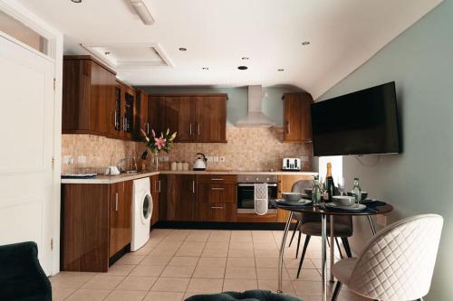 cocina con armarios de madera, mesa y TV en Cottage Lawn Apartment, en Enniskillen