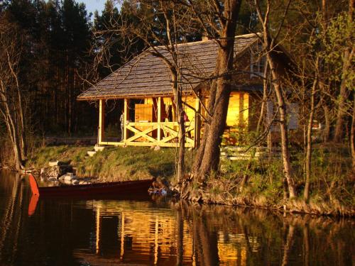 una casa a orillas de un río con un barco en Lakefront Log House and Sauna, en Ginučiai