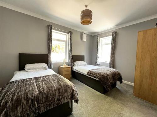 a bedroom with two beds and two windows at High Gables Apartment 2 in Paignton