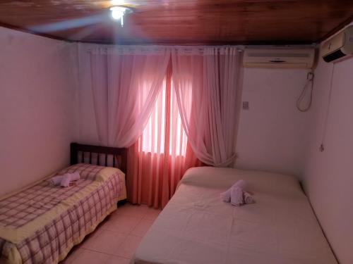 two beds in a room with a window with pink curtains at Los Olivos in Puerto Iguazú