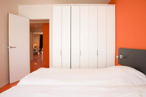 a bedroom with a white bed and an orange wall at Alfa Inn in Blankenberge