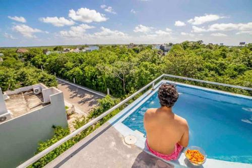 a man sitting on a balcony overlooking a swimming pool at CASA 24 PAX A 5 MIN DE LA PLAYA in Puerto Morelos