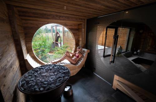 une femme assise sur un lit dans une pièce avec une fenêtre ronde dans l'établissement Hôtel-SPA Le Moulin De La Wantzenau - Strasbourg Nord, à La Wantzenau