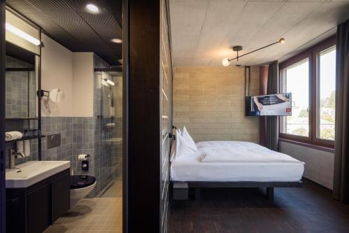 a bedroom with a bed and a bathroom with a tv at Tailormade Hotel LEO St Gallen in St. Gallen