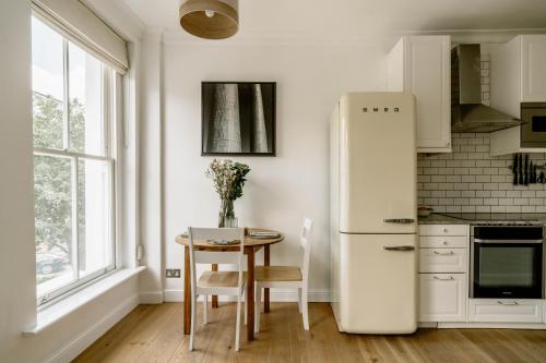 a white kitchen with a table and a refrigerator at Design-led flat in Camden on quiet street in London