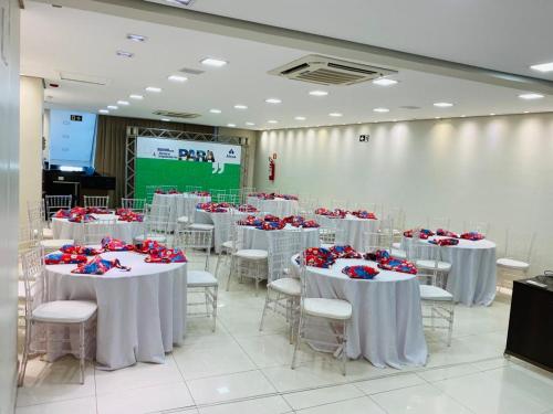 a room with white tables and chairs with red flowers on them at Hotel Palace Santarém Brasil in Santarém