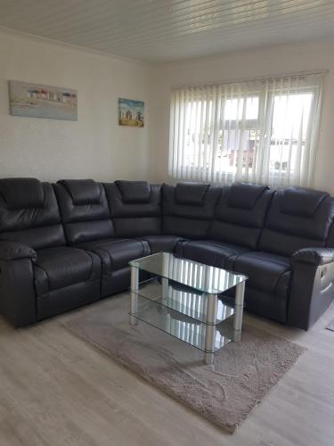 a living room with a black leather couch and a glass table at Summer Days in Camber