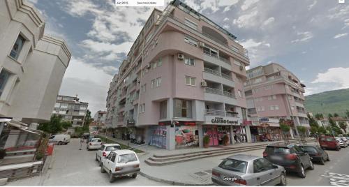 奥赫里德SM Apartment Center的一栋粉红色的高楼，街道上停满了汽车