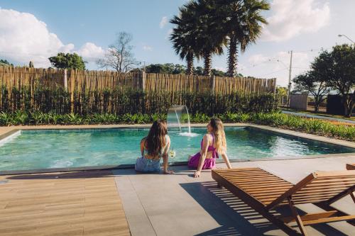 two girls are sitting next to a swimming pool at Espaço Paraíso Ortigueira in Ortigueira