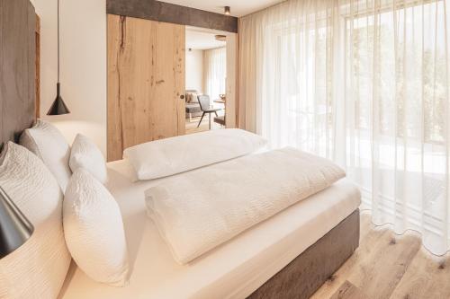a bedroom with a bed with white sheets and a window at Apartments Silva Living in San Giovanni in Val Aurina