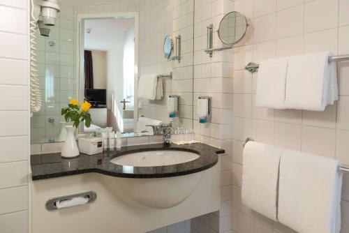 ein Badezimmer mit einem Waschbecken, einem Spiegel und Handtüchern in der Unterkunft Essential by Dorint Berlin-Adlershof in Berlin