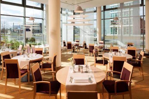 un restaurante con mesas, sillas y ventanas grandes en Essential by Dorint Berlin-Adlershof, en Berlín