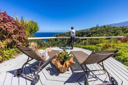 a man and a woman standing on a deck with chairs at Waterfall House with Ocean Views in Haiku, Maui in Huelo