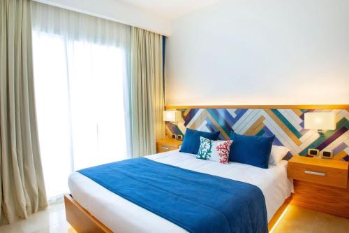 1 dormitorio con cama con sábanas azules y ventana en Cana Rock Condos Penthouse Vista Espectacular Golf & Jacuzzi B-336 y B-330, en Punta Cana