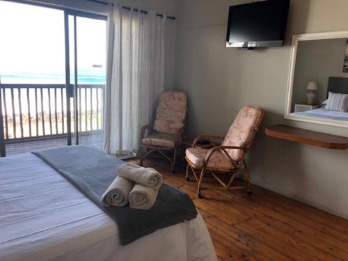 een slaapkamer met een bed en 2 stoelen en een televisie bij 14@Mitford in Morganʼs Bay