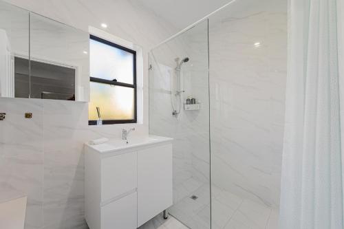 y baño blanco con lavabo y ducha. en Belmore Brand new renovated 3Br house AC & Parking, en Sídney