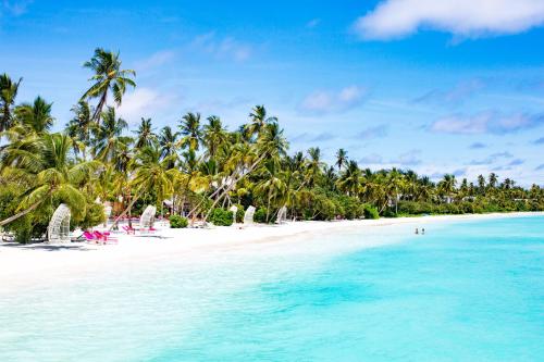 a beach with palm trees and turquoise water at Kandima Maldives in Kudahuvadhoo