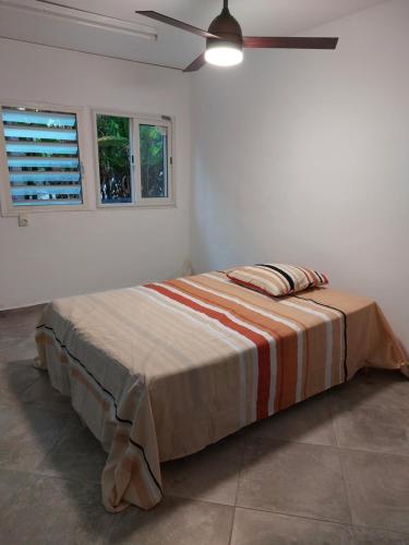Una cama en una habitación blanca con un ventilador de techo. en LA TERRASSE DES TORTUES, en Bouillante