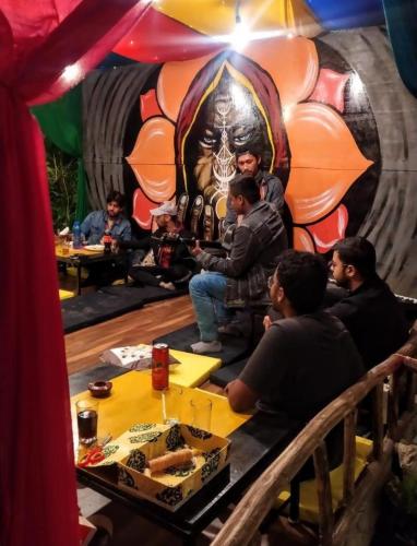 a group of people sitting at a table in front of a mural at Farm Hostel & Camps in Manāli