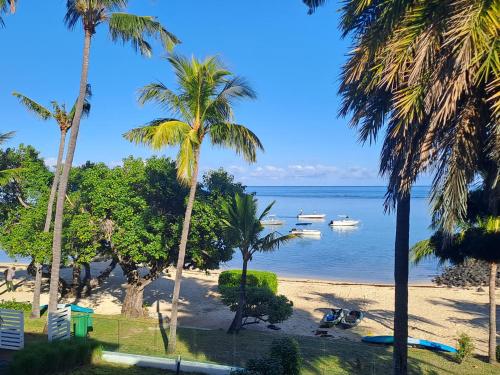 a beach with palm trees and boats in the water at CAPLAGE - BEACHFRONT GROUND FLOOR APARTMENT in TAMARIN in Tamarin