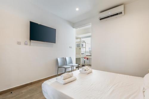 a white bedroom with a bed and a flat screen tv at Studio 42 with kitchenette at the new Olo living in Paceville
