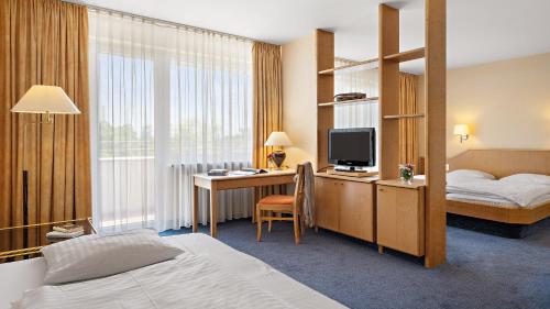 ミュンヘンにあるStyles Hotel Unterföhringのベッド、デスク、テレビが備わるホテルルームです。