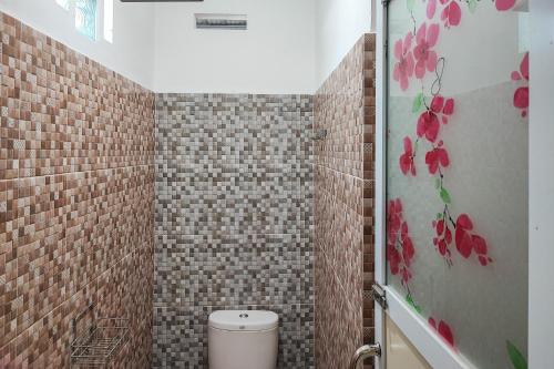 a bathroom with a toilet and a tiled wall at RedDoorz Syariah @ Penginapan Citra Alam 2 in Sungaitutung