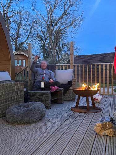 a woman sitting on a chair on a deck with a glass of wine at Southwell Retreat Glamping Pods in Southwell