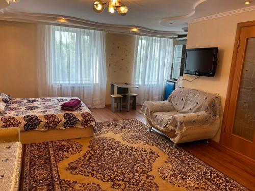 ein Schlafzimmer mit einem Bett, einem Stuhl und einem TV in der Unterkunft Уютная квартира Н.Абдирова 32 in Qaraghandy