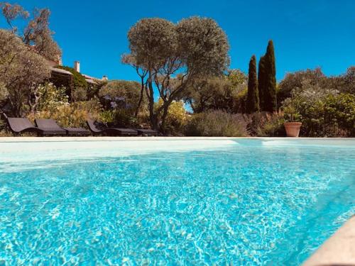 a pool of blue water with chairs and trees at Mas de la Beaume in Gordes
