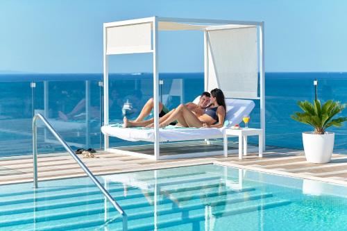three women sitting on a bed next to a swimming pool at Iberostar Selection Santa Eulalia Adults-Only Ibiza in Santa Eularia des Riu