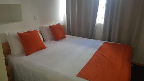 a bed with orange and white pillows and a window at Al-Xelb guesthouse in Silves