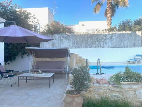 un patio con mesa, sombrilla y piscina en La maison les pins Chambre d'hote chez l'habitant en La Marsa