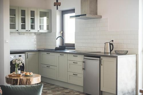 a kitchen with white cabinets and a sink and a table at Dziewięćsił &Chaber _domki blisko lasu in Grywałd