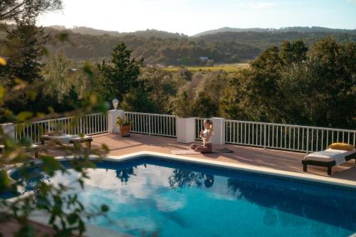 une femme assise sur une terrasse à côté d'une piscine dans l'établissement Oasis Living Villa Can Ramon, à Cala Llonga