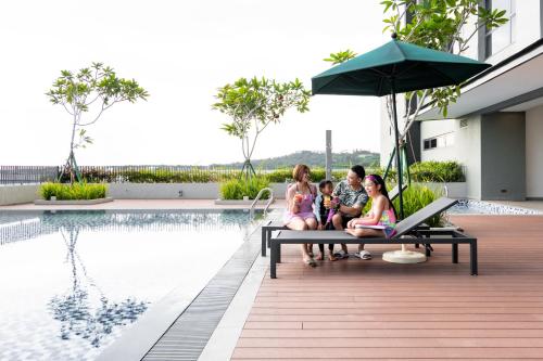 a family sitting on a bench next to a swimming pool at Holiday Inn Sepang - Airport in Sepang