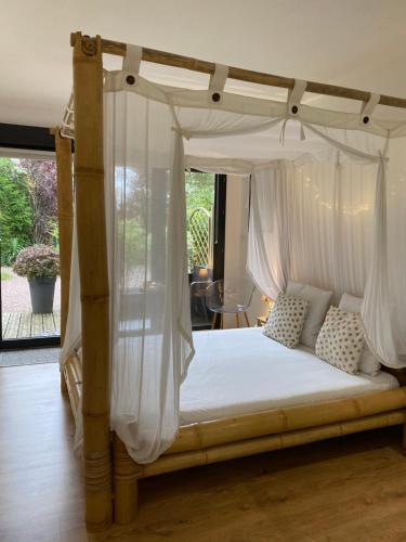 L'Hôtié de Brocéliande à Paimpont, au coeur des sites naturels et légendaires في بيامبونت: غرفة نوم مع سرير مظلة مع ستائر بيضاء
